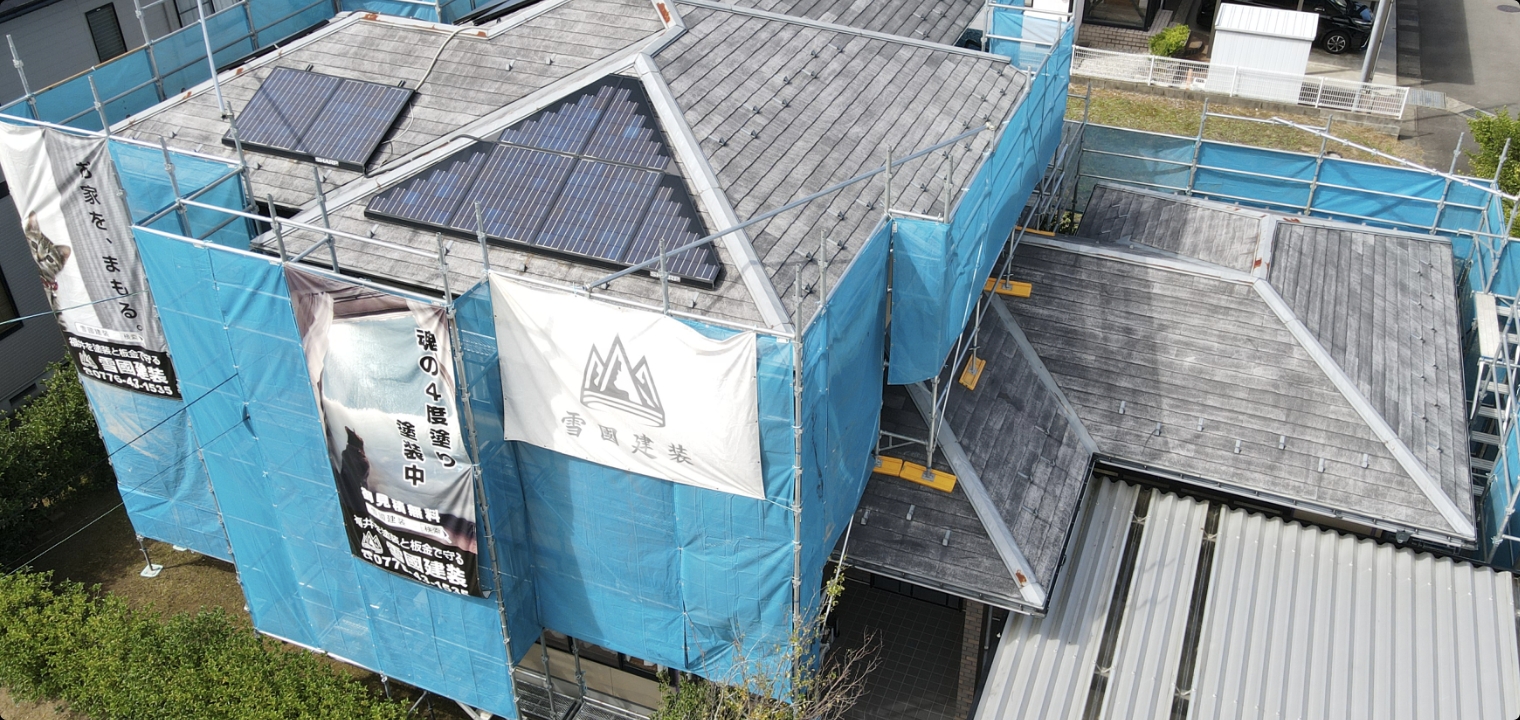 雪國建装の幕と青い養生ネットを張った、住宅の施工現場